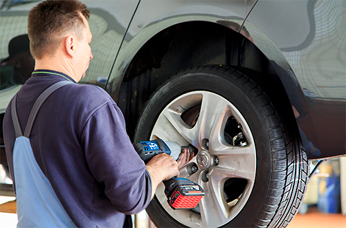 Mitarbeiter montiert Reifen an Auto auf Hebebühne